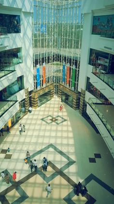 people are walking around in the lobby of a large building with many windows on each side