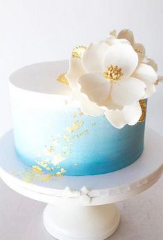 there is a blue and white cake with flowers on the top, sitting on a stand