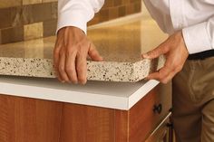 a man in white shirt and khaki pants standing next to counter with granite top