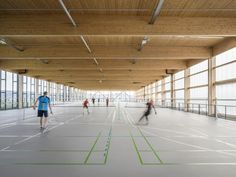 several people are playing basketball in an indoor court with large windows and wood ceilinging