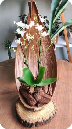 a wooden vase with flowers in it on top of a wood table next to a potted plant