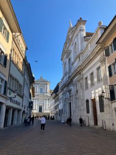 people are walking down the street in an old european city with white buildings and blue sky