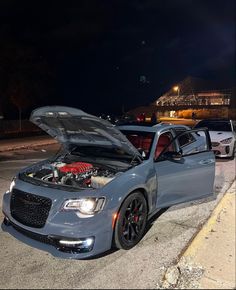 a car with its hood open parked on the side of the road at night time