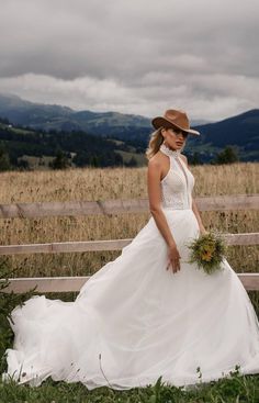 a woman in a white dress and hat standing by a fence