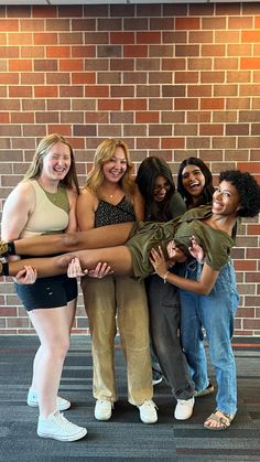 four girls are standing together in front of a brick wall and posing for the camera