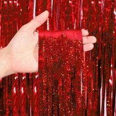 a hand holding a red piece of cloth in front of sequins and streamers