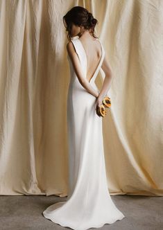 a woman standing in front of a curtain wearing a white dress and holding a flower