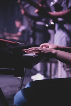 a person sitting at a piano with their hands on the keyboard and other people in the background