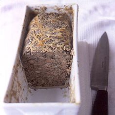 a loaf of bread in a white container next to a knife