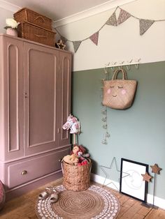 a room with pink and green walls, wicker baskets on the floor and a wooden cabinet