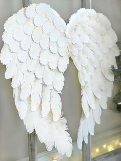 a white angel wings hanging on a window sill in front of a christmas tree