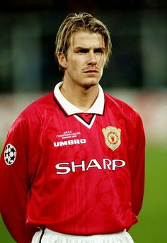 a young man in a red shirt standing on a soccer field with his hands behind his back