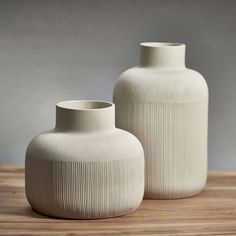 two white vases sitting on top of a wooden table