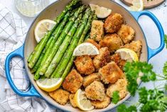 a pan filled with chicken and asparagus next to lemon wedges on a table