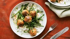 two plates filled with meatballs and green beans on top of rice next to silverware