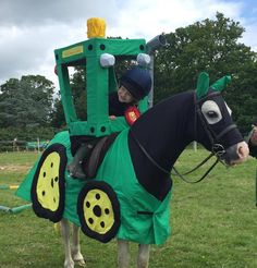 a young boy riding on the back of a horse wearing a green tractor shaped costume