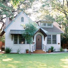 a small white house with a brown door and windows in the front yard is surrounded by trees