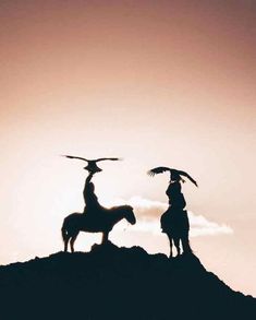 two people standing on top of a hill with an eagle flying above them and one person sitting on a horse