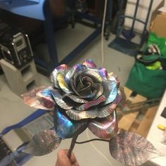 a person holding a metal rose in their hand with other items around the room behind them