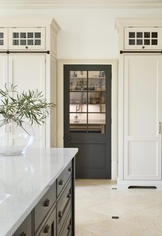 a kitchen with white cabinets and black doors in front of the door is a vase with an olive branch