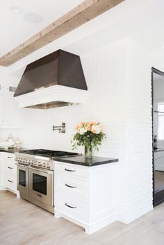 a kitchen with white cabinets and black counter tops, stainless steel range hood over the stove