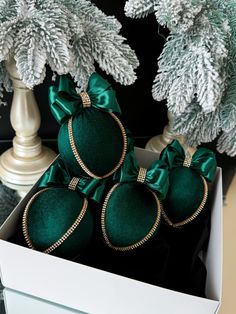 four green ornaments in a white box on a table next to christmas trees and other holiday decorations