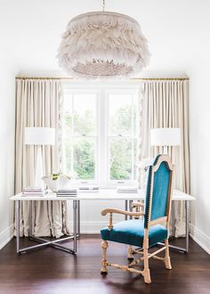 a blue chair sitting in front of a window next to a table with a lamp on it