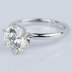 a white gold engagement ring with a round brilliant cut diamond in the center, on a gray background