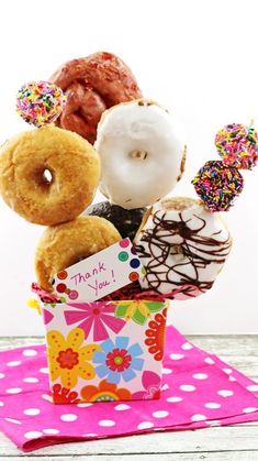 a box filled with assorted donuts on top of a pink table cloth next to a white wall