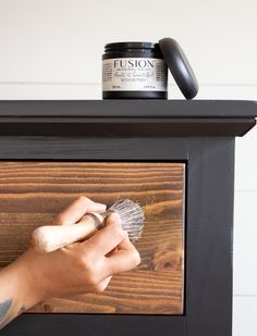 a person using a brush to paint a piece of wood on top of a dresser