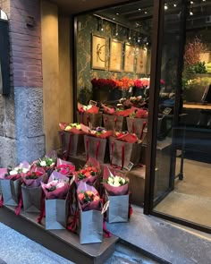 many bags with flowers in them sitting on the sidewalk outside a store front window,