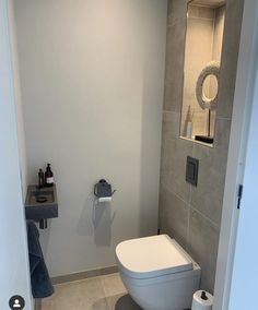 a white toilet sitting in a bathroom next to a sink under a mirror and towel dispenser