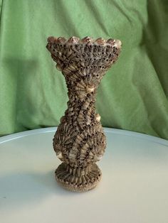 a vase made out of shells sitting on top of a white table next to a green cloth