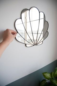 a hand holding a mirror over a wall with a shell shaped mirror on it's side