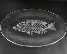 a glass plate with a fish etched on the front and bottom, sitting on a black surface