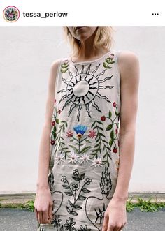 a woman standing in front of a white wall wearing a dress with flowers on it