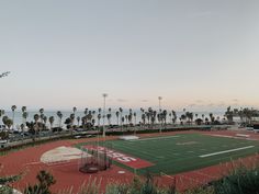 an empty football field with palm trees and the ocean in the backgrouds