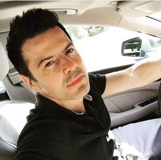 a man sitting in the driver's seat of a car with his hand on the steering wheel