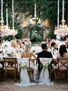 a bride and groom sitting at a table with chandeliers hanging from the ceiling