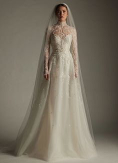 a woman in a wedding dress with a long veil on her head, standing against a gray background