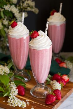 strawberry milkshakes with whipped cream and strawberries on a wooden tray next to flowers