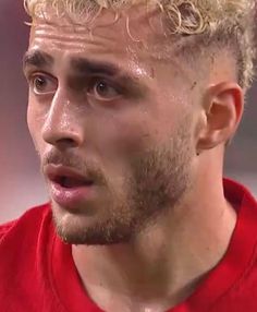 a close up of a man with blonde hair wearing a red shirt and looking off to the side