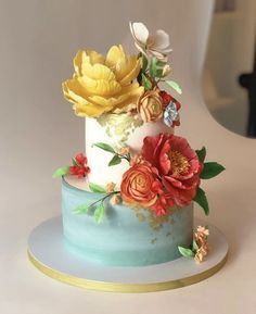 a three tiered cake decorated with flowers and gold trimmings on a white table