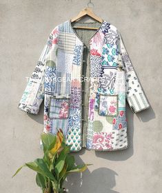 a patchwork jacket hanging on a wall next to a potted plant with green leaves