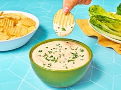 a person dipping chips into a bowl of ranch dip with lettuce on the side