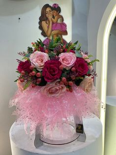 a pink flower arrangement on top of a white pedestal in front of a wall with an image of a woman