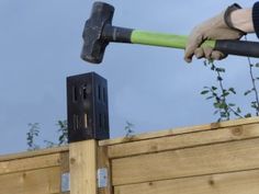 a person holding a hammer over the top of a wooden fence