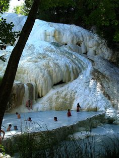 several people are swimming in the water near some ice covered rocks and trees with snow on them