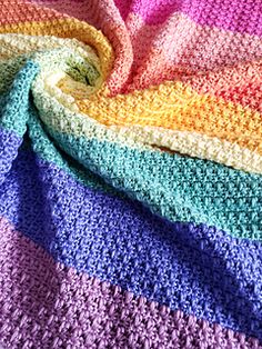 a multicolored crocheted blanket is laying on top of a bed sheet