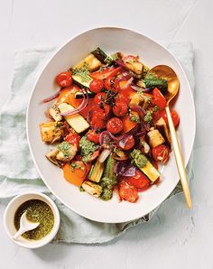 a white bowl filled with vegetables next to a small bowl of seasoning and spoons